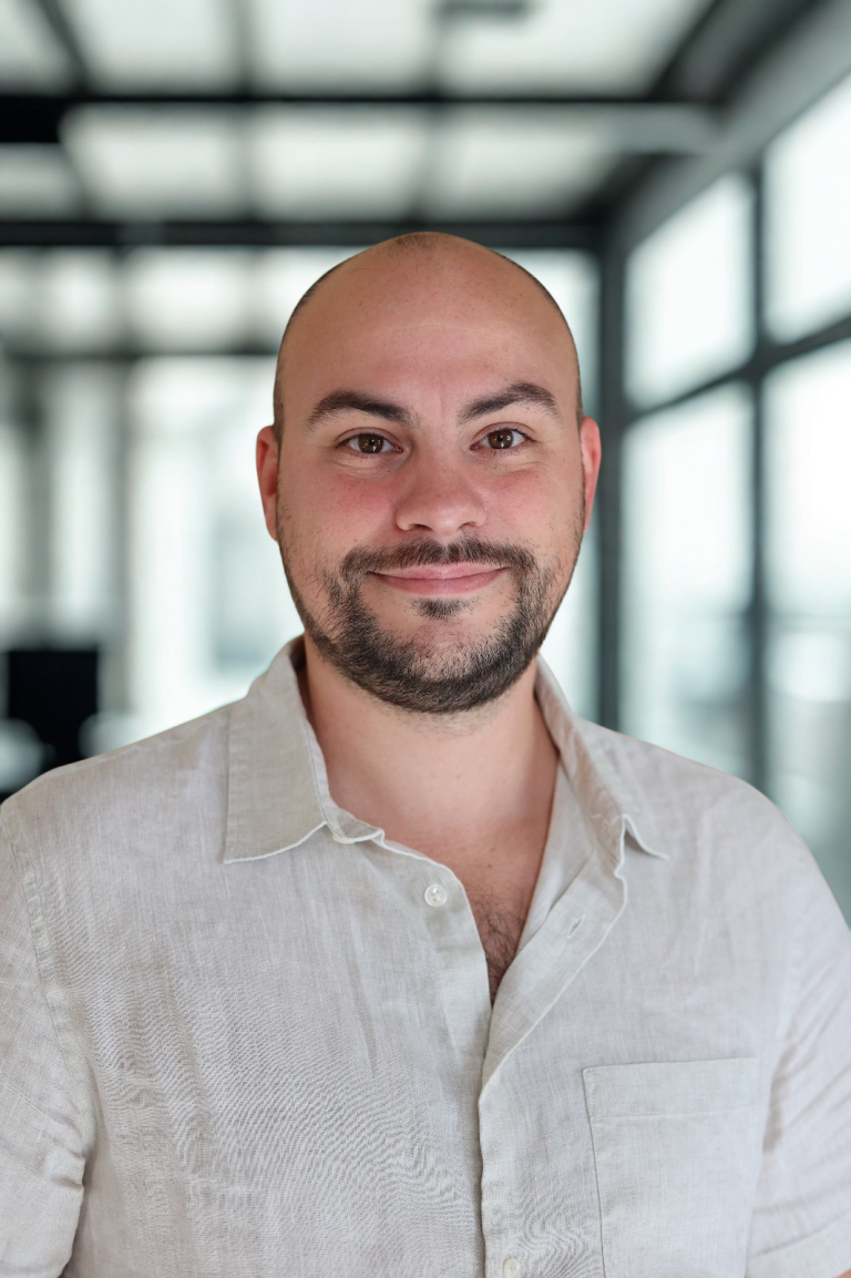 Portrait d'un homme chauve souriant en chemise beige clair.